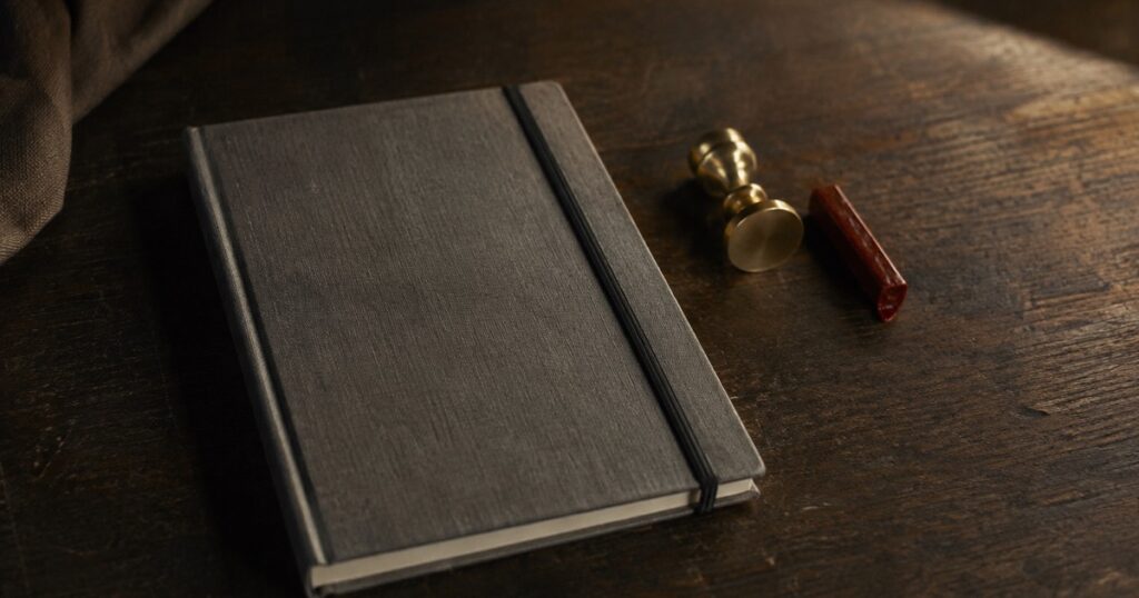 Un cuaderno cerrado con una goma junto a un sello de lacre sobre un escritorio