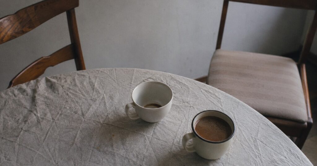 Dos tazas en una mesa, una vacía y la otra llena y fría, con las sillas apartadas