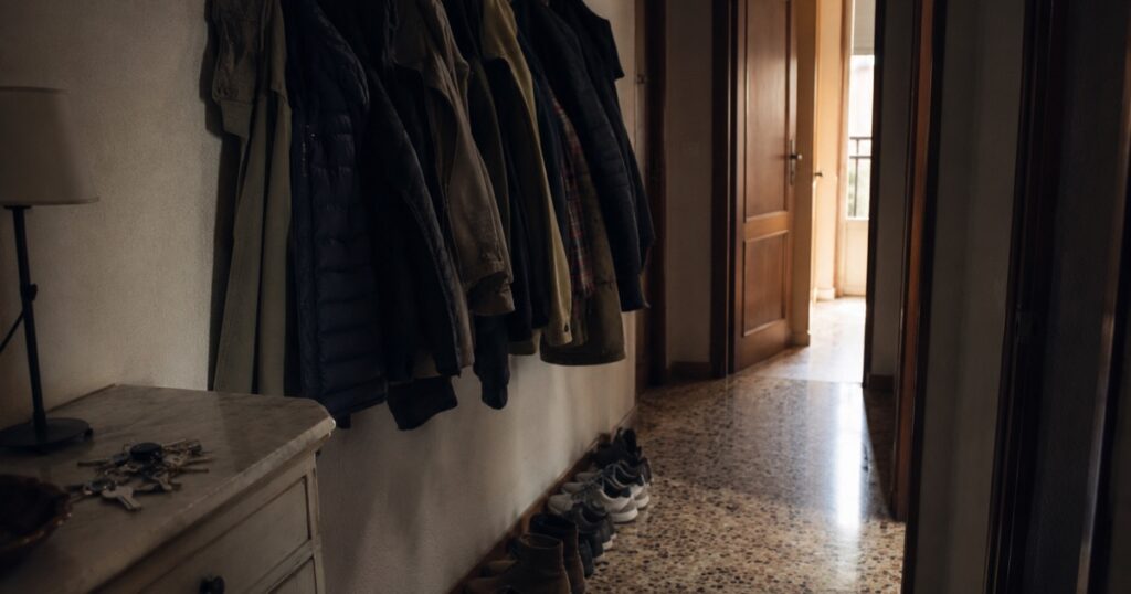 Recibidor de un piso con muchos abrigos colgados y varios pares de zapatos