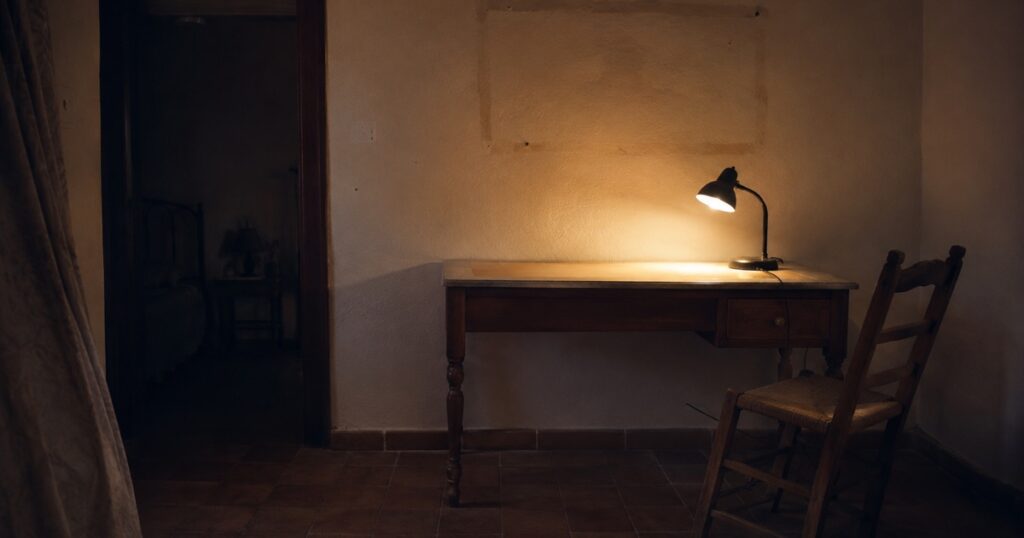 Un escritorio vacío con la lámpara encendida y la silla apartada