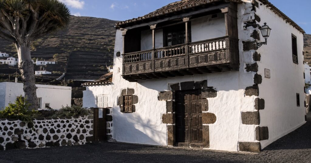 Casa canaria de cal blanca con esquinas de piedra volcánica negra y balcón de madera