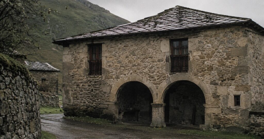 Casa montañesa de piedra con dos arcos en la planta baja bajo el cielo gris