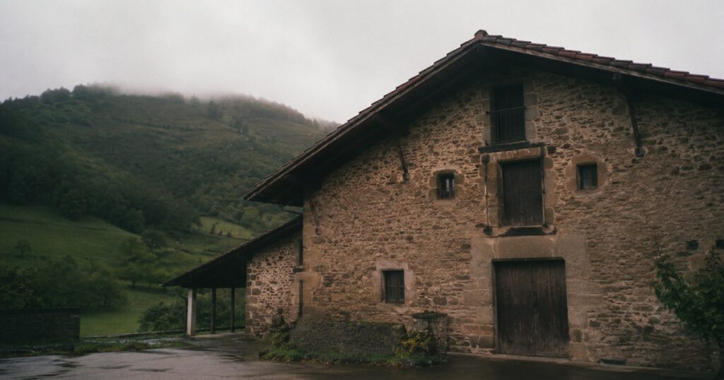 Caserío vasco de piedra con el tejado de aleros anchos y colinas verdes al fondo